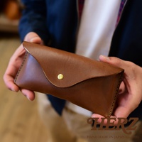 職人手作的咖啡色皮革眼鏡收納盒，以簡約的造型搭配金色金屬釦，由雙手拿取展示。