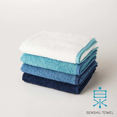 SOLID 細柔蓬韌緞澤長纖浴巾，堆疊展示四種不同深淺的藍色調，材質觸感蓬鬆，邊緣帶有織紋裝飾。