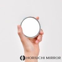 一隻手拿著一個圓形口袋小鏡子，鏡面為白色，外框有彩色圖案，鏡子邊緣為銀色金屬材質。