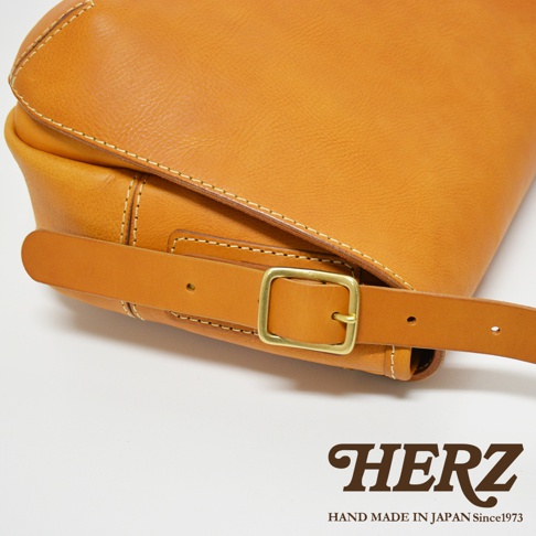 職人手作復古翻蓋郵差包，採用天然皮革製成，呈現溫潤的焦糖棕色。包款設有可調節的皮質背帶，配有黃銅色金屬針釦，展現經典工藝。