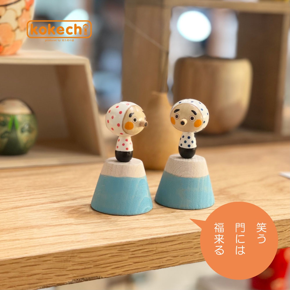 兩尊木芥子開運擺飾，分別為富士山與火男造型。富士山造型為藍色底座，火男造型為白色底座。皆為木質，頭部飾有紅點或藍點圖案，臉部有圓形紅臉頰。