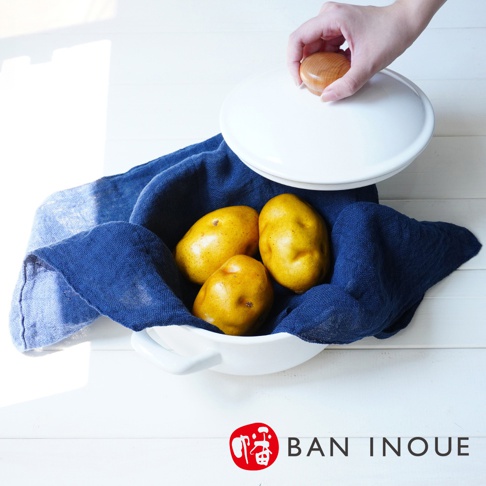 BAN INOUE 品牌標誌旁，有白色的鍋子，裡面盛著三顆黃色的馬鈴薯，被深藍色的布巾包裹著，鍋蓋由一隻手拿著。