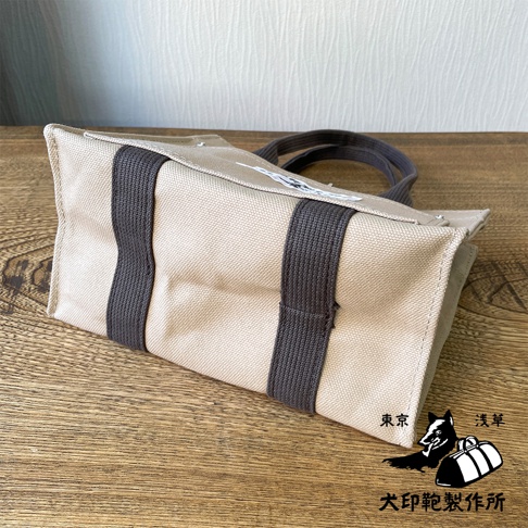 犬印純棉帆布迷你托特包，米白色帆布材質，搭配深灰色織帶裝飾及提把，包面印有黑白狗與行李袋圖案。