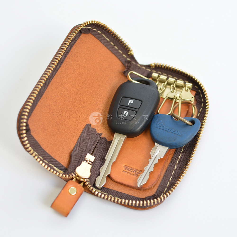 開啟的棕色皮革鑰匙包，裡面裝有兩把鑰匙，一把是黑色汽車鑰匙，另一把是藍色鑰匙。