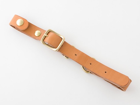 職人手作皮革背包用減壓胸前扣帶，採用 tan 色皮革製成，配有黃銅色針扣、鉚釘和 D 型環，用於調整和固定。