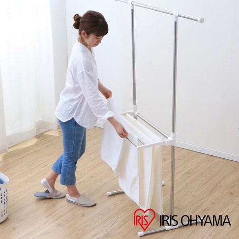 一位女性正在組裝不鏽鋼曬衣架，曬衣架為銀白色，有兩層曬衣桿，可掛多件白色毛巾。