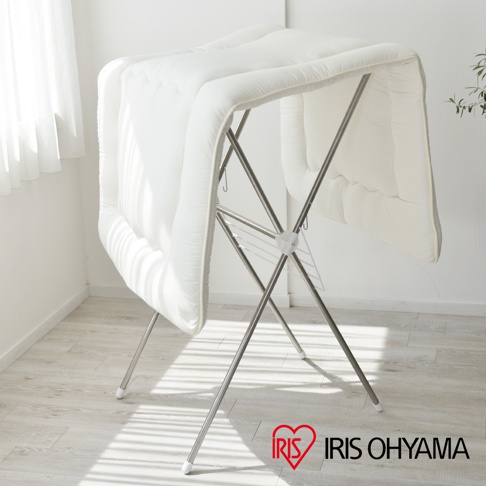 一個白色厚實的棉被蓋在銀色的金屬曬衣架上，曬衣架為 X 形結構，有兩層橫桿，頂端有白色塑膠連接件。