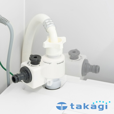 白色與灰色相間的Takagi洗衣機分水轉接頭安裝在洗衣機上，裝置上方接有白色進水軟管，兩側配有旋轉開關與接水口，整體設計簡潔，用於將水流導入洗衣機。