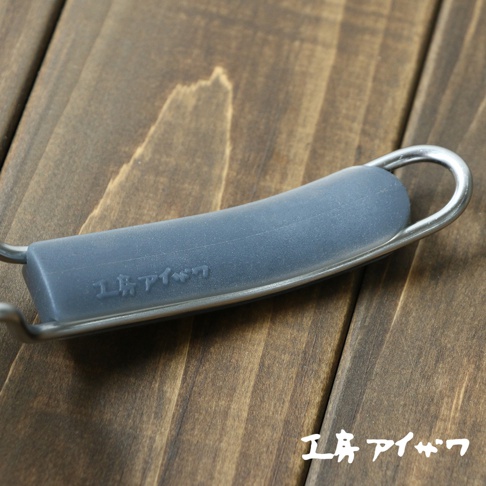 不鏽鋼濾網的灰色矽膠握柄，握柄上有日文壓印，金屬框架環繞握柄，背景是深色木紋桌面。