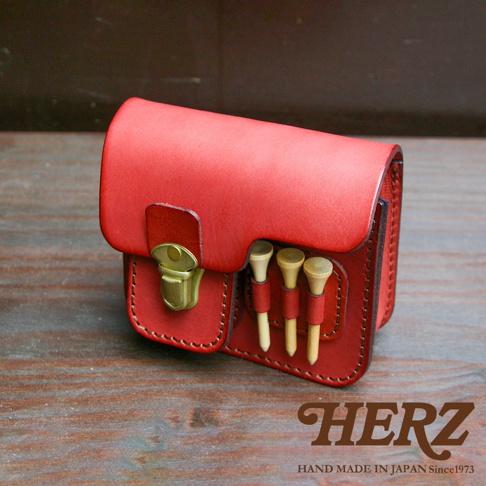 紅色皮革高爾夫腰包，附有黃銅扣和三個高爾夫球釘插槽，手工縫製，展現職人精神。
