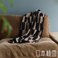 日本桃雪户外格纹棉柔迷你浴巾，带有标志性的格子图案，搭在条纹纹理的棕色沙发上。
