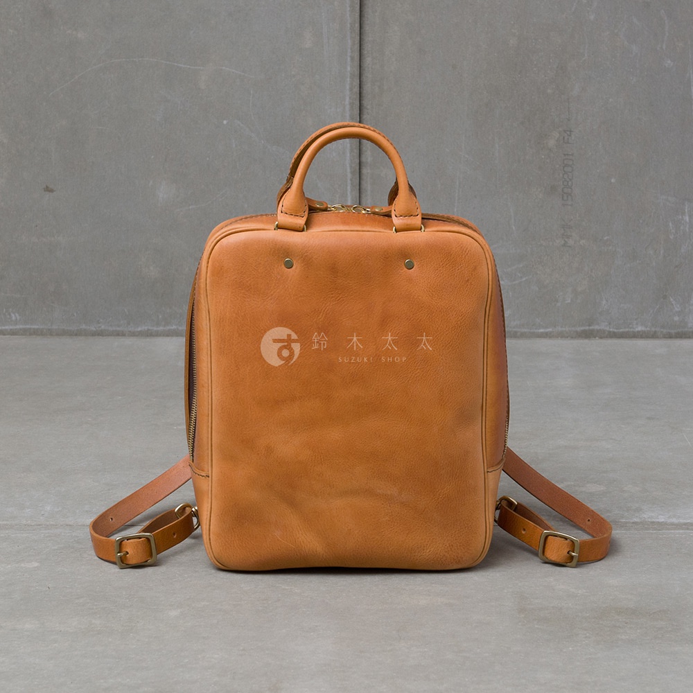 職人手作皮革Organ商務後背包 M-10，採用溫潤的棕褐色皮革製作，方正的包型設計，配有雙提把和可調整的側背帶，包身中央有品牌標誌。