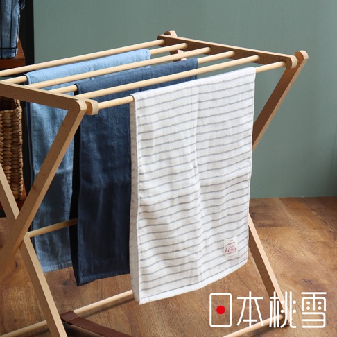 木製晾衣架上掛著三條紗布毛巾，分別為淺藍色、深藍色和白色條紋。