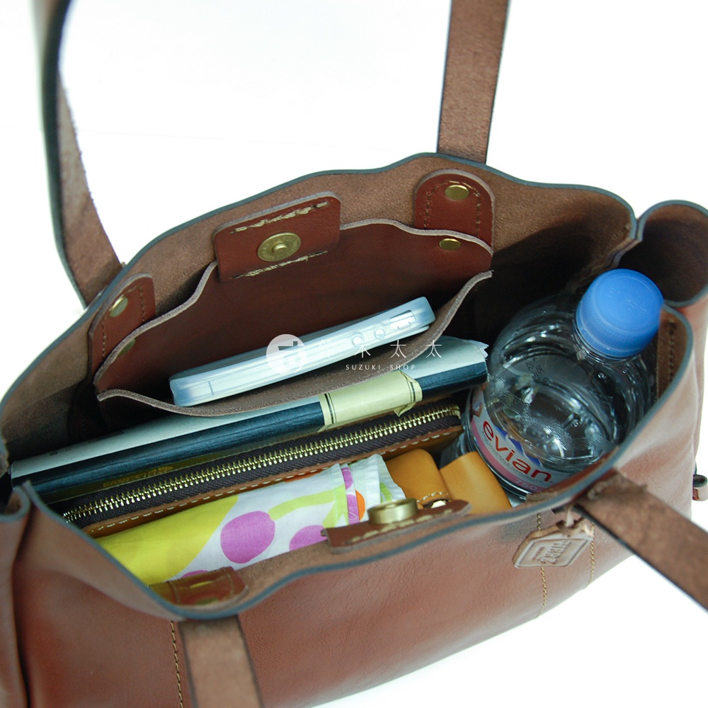 職人手作棕色皮革仕女托特包，內部可見手機、水瓶、筆和摺疊傘，包款設計簡約實用。