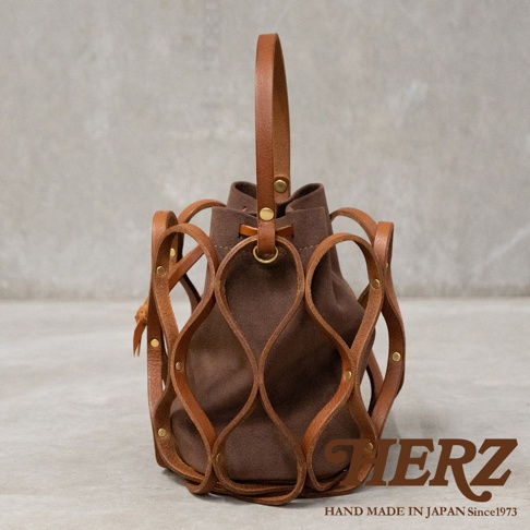日本HERZ職人手作皮革Organ編織水桶包 G-98，採用棕色絨面革內袋搭配皮革編織網罩，提把處有金色五金裝飾，底部印有HERZ LOGO及HAND MADE IN JAPAN Since 1973字樣