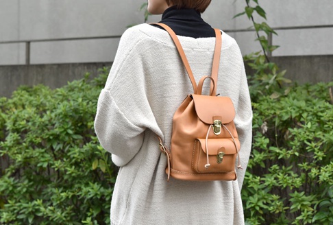 皮革經典迷你後背包，採用淺棕色皮革製作，帶有翻蓋設計，下方有一個小前袋，以抽繩和金屬扣鎖固定。