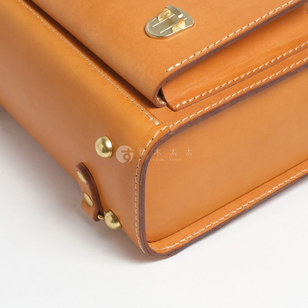 職人手作皮革橫式書包的側邊細節，帶有黃銅色的鎖扣和鉚釘，以及清晰的手縫白色縫線。