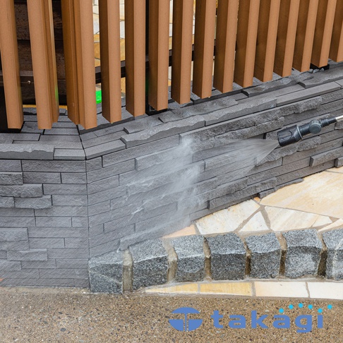 takagi 品牌標誌和旋噴頭正在噴水清潔石牆。