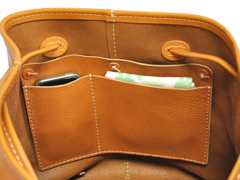 職人手作皮革可調式兩用大容量托特包內部，展示了棕褐色皮革材質，包含一個手機隔層與一個放置物品的袋口，以及束繩設計。