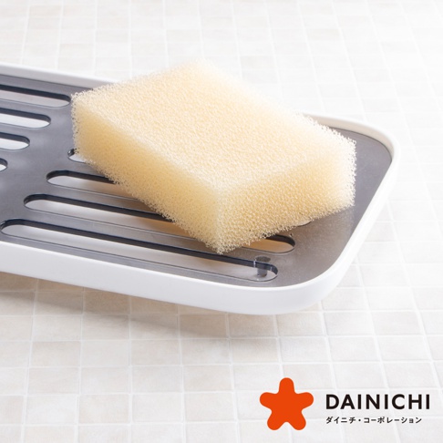 淺黃色海綿靜置於白色塑膠與灰色金屬材質的瀝水架上，海綿表面紋理細密。