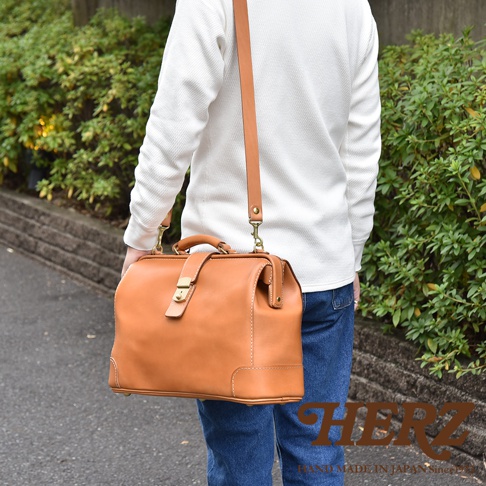 淺棕色皮革製成的公事包，帶有手柄和可拆卸肩帶，側面有縫線細節，並配有金色金屬鎖扣。