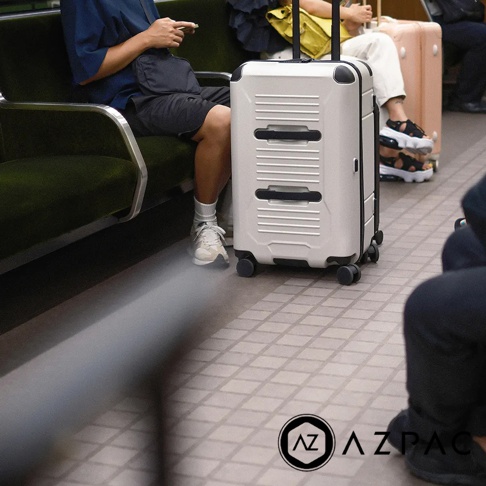 AZPAC Trucker 2.0 26吋旅行箱，白色硬殼材質，設有兩段式黑色拉桿和四個萬向輪。箱體表面有橫向條紋設計，並有兩個黑色嵌入式提把。