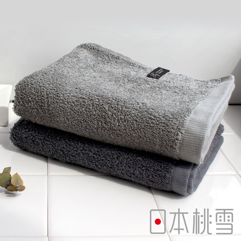 兩條厚實的毛巾疊放，上方為淺灰色，下方為深灰色，皆為純棉材質。