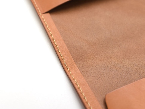 淺棕色皮革翻蓋記事本書套，特寫縫線細節，內裡為絨面皮革。