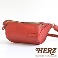 紅色職人手作皮革輕便斜背包，設有金色拉鍊及品牌標誌。