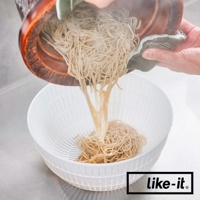 一個白色雙層塑膠瀝水籃，正在從一個木製容器中瀝乾蕎麥麵。