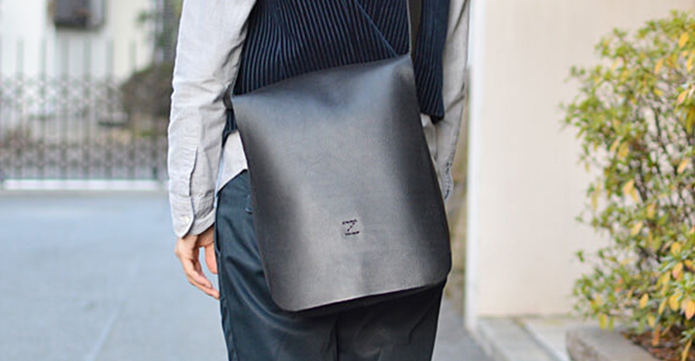 男人斜背著一個黑色軟皮直式斜背包，包身上有一個小小的「N」字 Logo