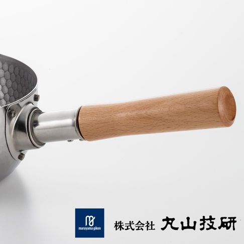 丸山技研不鏽鋼雪平鍋的局部特寫，展示了帶有蜂巢狀紋路的金屬鍋身，以及與鍋體連接的圓柱狀金屬柄，末端銜接淺色原木手柄，整體設計簡約實用，並於底部標示品牌標誌與丸山技研中文字樣。