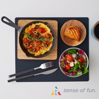 黑色耐高溫微波爐防污保護墊上，擺放著一個鑄鐵鍋，鍋中盛有番茄、橄欖和迷迭香裝飾的烘蛋；旁邊有一個木盤，上面放著一個酥皮派；下方有一個透明碗，裝有番茄、奶酪和綠葉蔬菜組成的沙拉；另外還有銀色金屬叉和刀，手柄為黑色。