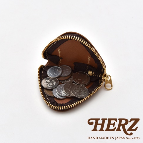 一個造型獨特的日本HERZ手工棕色皮革三角飯糰零錢包，拉鍊呈現半開狀態，內部裝有多枚日本硬幣，白色背景右下角印有HERZ品牌商標與產地說明。