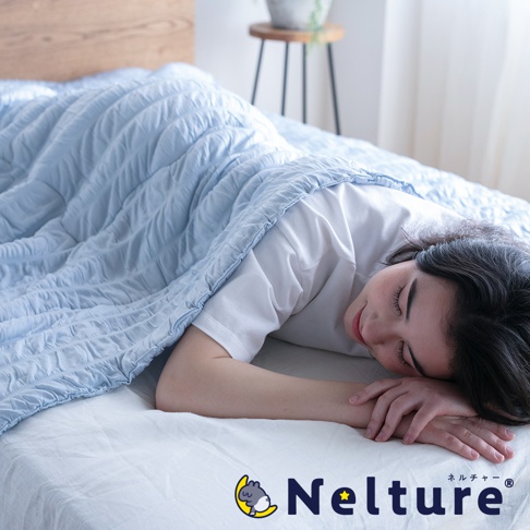 淺藍色 Nelture 單人涼感被，被面有壓紋設計，蓋在一位側臥的女性身上，她身著白色 T 恤，臉部表情安詳，雙手放在臉頰旁。