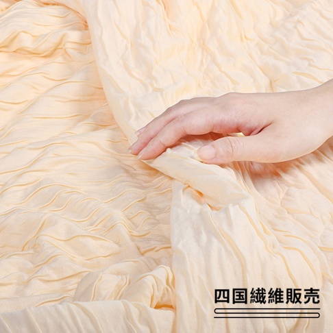 淺黃色舒芙蕾透氣涼被，材質輕盈，表面有獨特的壓褶紋理，手部觸感展示其柔軟蓬鬆的質感。