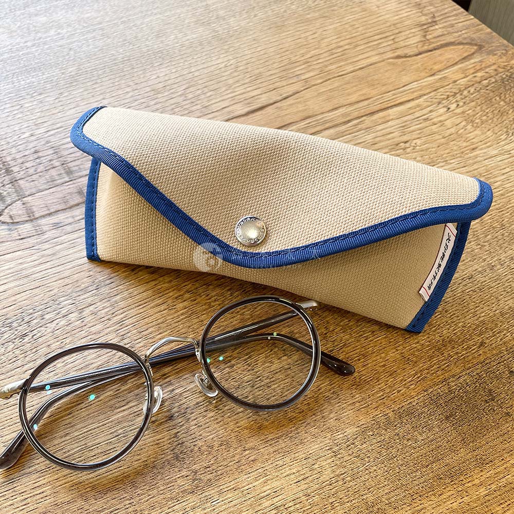 犬印純綿帆布眼鏡收納盒與一副圓形鏡框眼鏡，兩者一同置於木質桌面。
