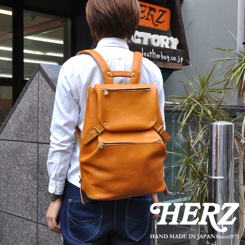 職人手作皮革多口袋後背包，顏色為天然棕色，採用高品質皮革製成，設有兩個拉鍊前袋和金屬扣環，展現經典復古風格。
