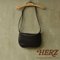 黑色皮革單肩半月包，附有可調式背帶和金色拉鍊，懸掛在木製衣架上。