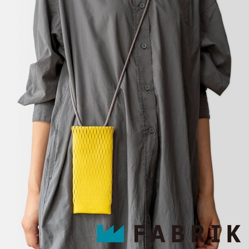 FABRIK 品牌的黃色皮革手機包，以其獨特的網狀皮革紋理設計，由模特兒身穿灰色連身裙展示。