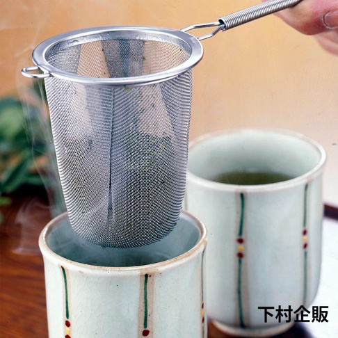 不鏽鋼濾茶網，網眼細密，帶有鋼絲手柄，正浸入裝有茶葉的茶杯中，杯身為白色，飾有綠色條紋和紅色、黃色小圓點。