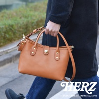 駝色皮革迷你托特包，附可拆卸斜背帶，正面有金屬釦和鉚釘裝飾，由職人手工製作。