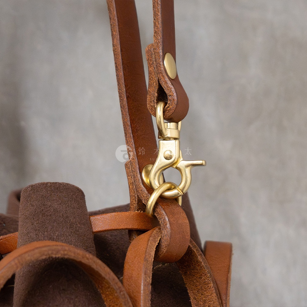 日本HERZ職人手作皮革Organ編織水桶包 G-98 的部分細節，特寫黃銅釦環與咖啡色皮革背帶。