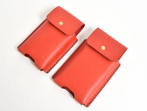 兩件式紅色皮革手機收納包，帶有金色按扣和縫線細節，設計簡潔。