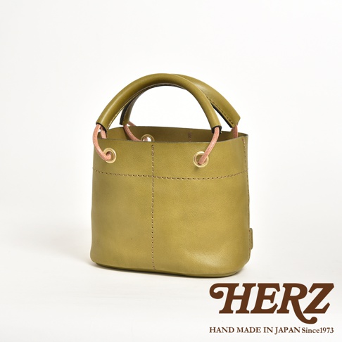 職人手作皮革加厚提把大開口午餐袋，呈現橄欖綠，束口設計搭配粉色細繩及金屬環，簡約大方。