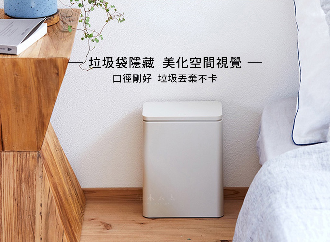 淺灰色方形按壓式垃圾桶，帶有簡潔的頂蓋，置於木質地板和白色牆壁之間。