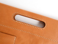 職人手作皮革橫式收納袋中袋，以淺棕色皮革製成，車縫線為白色。圖片特寫了袋子上的提把，提把開口處有精緻的縫線加固，袋身有多條平行車縫線，展現皮革的紋理與質感。