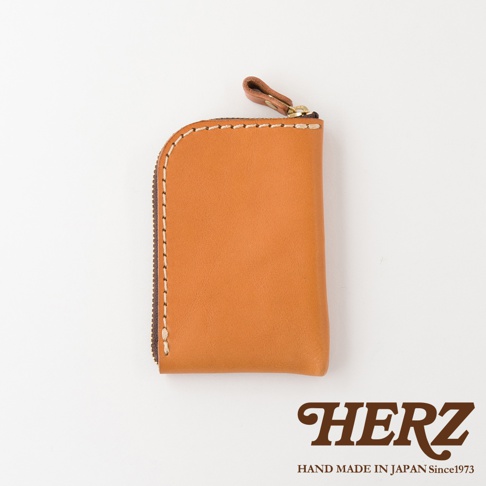 一個日本HERZ職人手作的棕色Stare皮革迷你零錢包，外觀為簡約的圓弧邊角設計，側邊配有拉鍊與皮革拉環，下方印有HERZ品牌標誌。