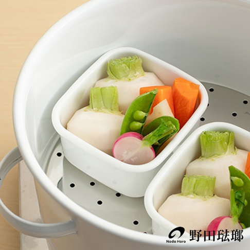 兩個白色方形琺瑯保存容器，內裝白蘿蔔、豌豆莢、紅蘿蔔塊和切半的櫻桃蘿蔔，置於蒸鍋內。
