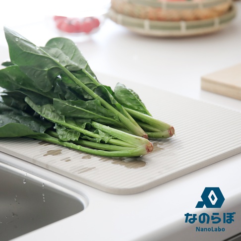 寬版淺灰色珪藻土置物墊上，擺放著一束新鮮的綠色菠菜，葉片上帶有水珠。墊子表面有細緻的條紋，靠近水槽，部分區域有水漬。